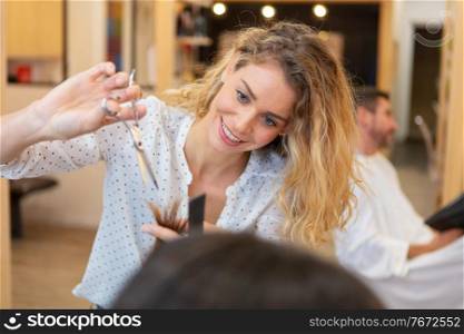 pretty hairdresser cutting hair tips of a female customer