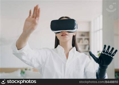 Pretty handicapped girl in virtual reality glasses touches the image. Young european woman in white shirt with artificial hand is excited. Futuristic medical 3d technology for rehabilitation.. Pretty handicapped girl in virtual reality glasses touches the image. 3d rehabilitation technology.