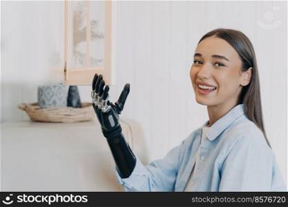 Pretty handicapped girl is opening cupboard at kitchen. Happy european woman with artificial arm at home. Functions of modern bionic prosthesis. Routine of disabled person concept.. Pretty handicapped girl is opening cupboard at kitchen. Happy european woman with bionic prosthesis.