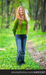 Pretty happy woman with red long hair walking in the green spring park
