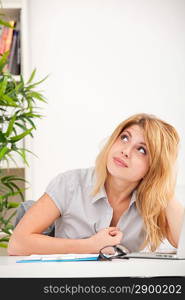 Pretty, happy, young woman in blouse looking up and sitting at the desk in the office
