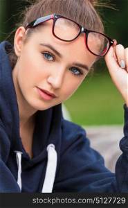 Pretty intelligent girl or young woman wearing glasses and lifting them to show her blue eyes