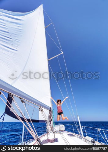 Pretty joyful woman in bright sunny day having fun on sailboat, jumping on the deck of luxury water transport, active summer vacation