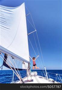 Pretty joyful woman in bright sunny day having fun on sailboat, jumping on the deck of luxury water transport, active summer vacation