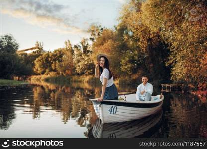 Pretty lady poses in boat on quiet lake at summer day. Romantic date, boating trip, man and woman walking along the river. Pretty lady poses in boat on quiet lake