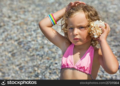 pretty little girl has leant seashell bowl to an ear on seacoast