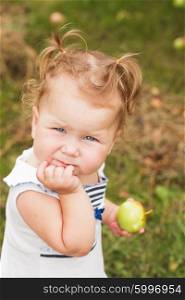 Pretty little girl holding an apple in hand, standing under the apple tree