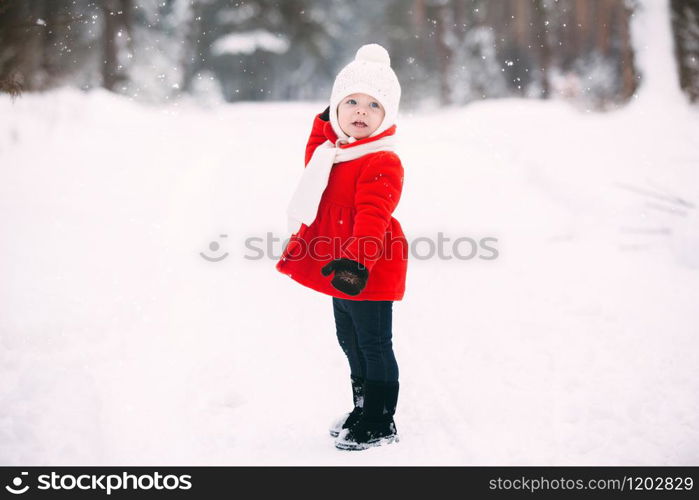 pretty little girl in red coat in winter forest. Little girl having fun on winter day. cheerful little baby girl in gloves and white hat runs on snow white