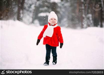 pretty little girl in red coat in winter forest. Little girl having fun on winter day. cheerful little baby girl in gloves and white hat runs on snow white
