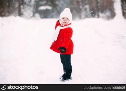 pretty little girl in red coat in winter forest. Little girl having fun on winter day. cheerful little baby girl in gloves and white hat runs on snow white