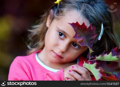 Pretty little girl with big eyes and autumn leaves looking seriously
