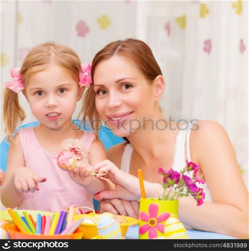 Pretty mother with cute little daughter painted Easter eggs at home, having fun indoor, spring holiday