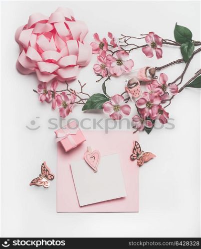 Pretty pastel pink greeting card mock up with blossom decoration, hearts, little gift box and bow on white desk background, top view, flat lay. Wedding invitation layout or Mother Day concept
