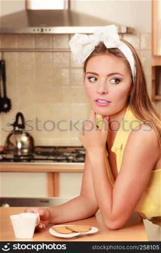 Pretty pin up girl with heart shape gingerbread cookies drinking tea or coffee at home. Gorgeous young retro woman with hot beverage relaxing in kitchen.. Girl with gingerbread cookies drinking tea coffee.