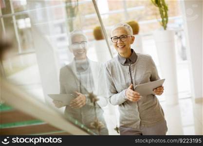 Pretty, positive, a≥d woman with beaming smi≤holding tab≤t in modern office