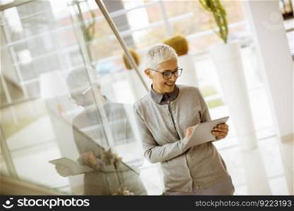 Pretty, positive, aged woman with beaming smile holding tablet in modern office