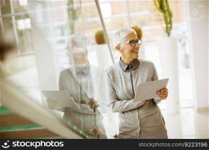 Pretty, positive, aged woman with beaming smile holding tablet in modern office