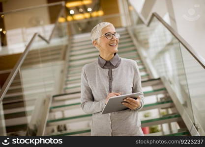 Pretty, positive, aged woman with beaming smile holding tablet in modern office