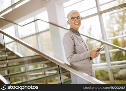 Pretty, positive, aged woman with beaming smile holding tablet in modern office