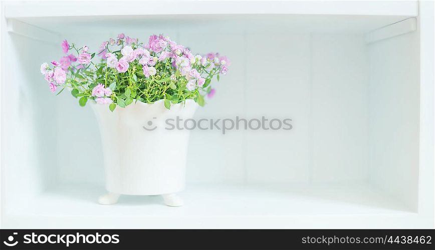 Pretty purple flowers in white pot on shelf. Light floral Home decoration and interior background.