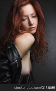 Pretty redhead young woman portrait with leather jacket pulled over shoulder exposing bare breasts.