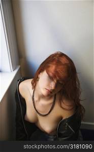 Pretty redhead young woman portrait with leather jacket pulled over shoulders exposing bare breasts.