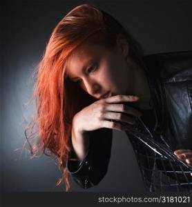 Pretty redhead young woman wearing leather jacket hanging over back of chair.
