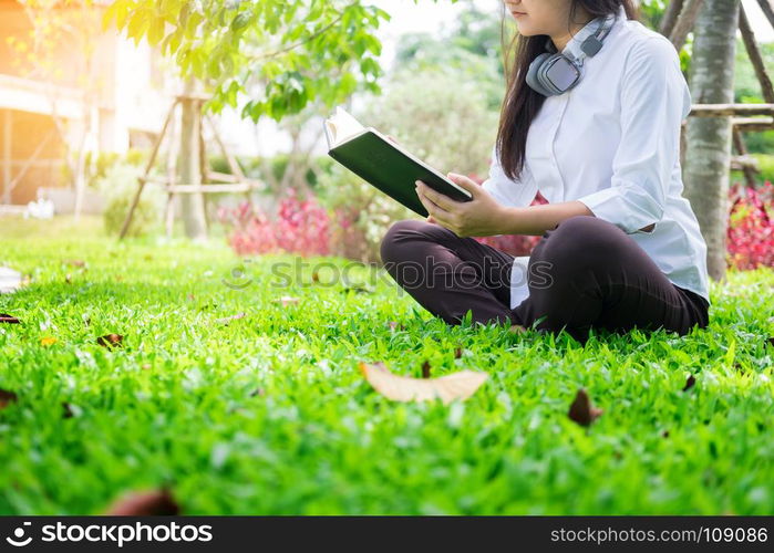 Pretty relaxed young beautiful woman reading a book in the garden lawn with sun shining