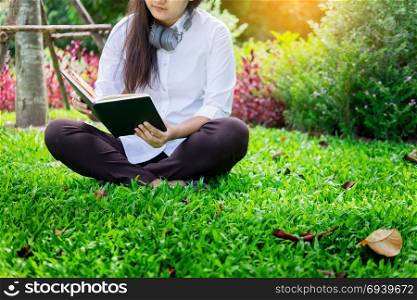 Pretty relaxed young beautiful woman reading a book in the garden lawn with sun shining