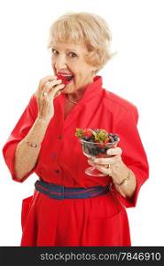 Pretty senior woman eating a bowl of healthy delicious mixed berries. Isolated on white.
