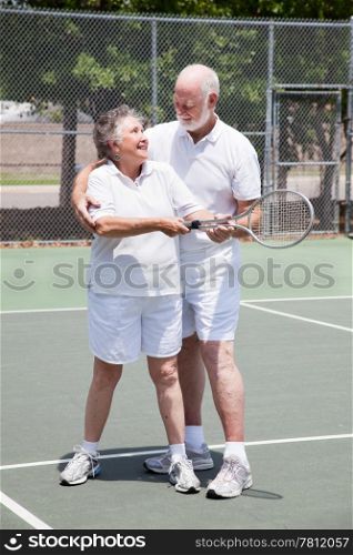 Pretty senior woman gets a tennis lesson from her handsome husband.