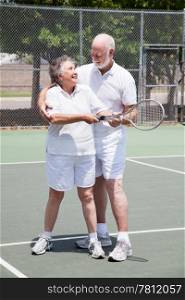 Pretty senior woman gets a tennis lesson from her handsome husband.