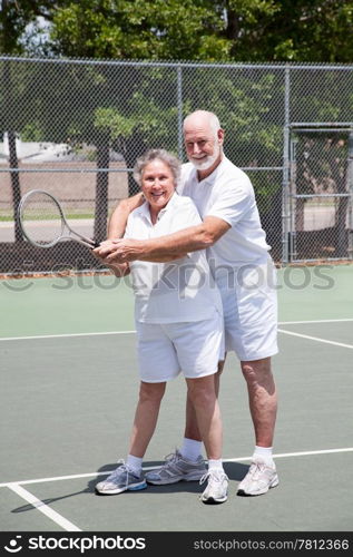 Pretty senior woman gets tennis instruction from a handsome senior man.