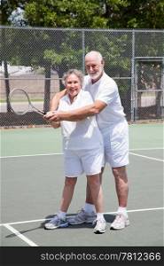 Pretty senior woman gets tennis instruction from a handsome senior man.