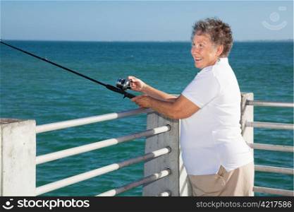 Pretty senior woman happily fishing from a pier.
