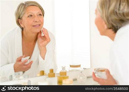 Pretty senior woman in bathroom looking at herself in mirror