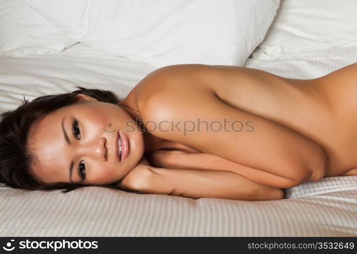 Pretty Singaporean woman lying nude in bed