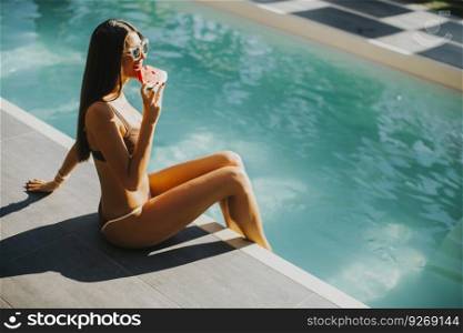 Pretty slim beautiful woman resting by swimming pool in swimsuit and eating watermelon at hot sunny day