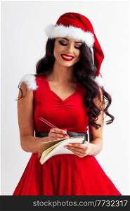 Pretty smiling beautiful Santa girl in red dress writing wish list. Santa girl writing wish list