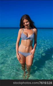 Pretty smiling girl in bikini standing in transparent water of tropical sea. Pretty girl in bikini at sea
