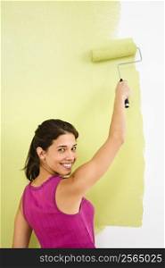 Pretty smiling woman painting interior wall of home with paint roller.