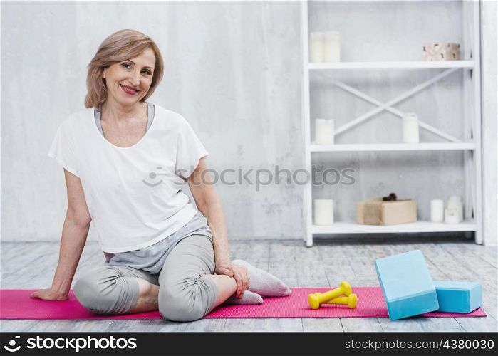 pretty smiling woman sitting near blocks dumbbells yoga mat