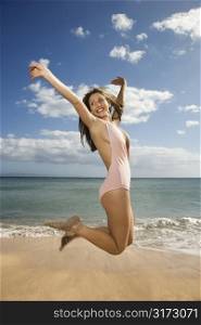 Pretty smiling young Caucasian woman in swimsuit jumping into air at beach in Maui Hawaii.