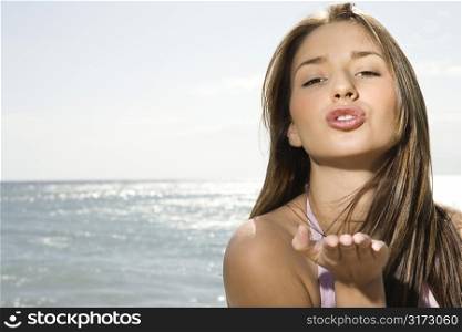 Pretty smiling young Caucasian woman with long brown hair blowing viewer a kiss at beach in Maui Hawaii.