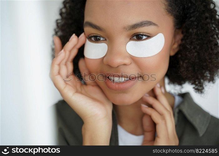 Pretty smiling young mixed race girl uses cosmetic moisturizing under eye patches, modern biracial teen lady does morning beauty procedures for healthy glowing facial skin. Skincare routine concept.. Pretty smiling young mixed race girl uses cosmetic moisturizing under eye patches. Skincare routine