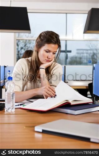 Pretty student, concentrating on a text book, studying in a library