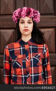 Pretty stylish girl with pink flower crown and red plaid shirt In front of a wooden door