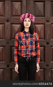 Pretty stylish girl with pink flower crown and red plaid shirt In front of a wooden door