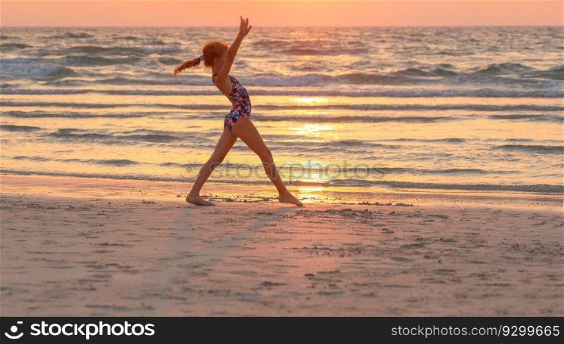 Pretty teen girl doing sport exercise on the beach over sunset sky background. Active sportive summer c&. Dancing near the sea. Healthy childhood.. Teen girl doing exercise on the beach