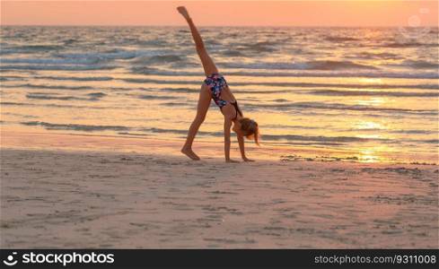 Pretty teen girl doing sport exercise on the beach over sunset sky background. Active sportive summer camp. Dancing near the sea. Healthy childhood.. Teen girl having fun on the beach